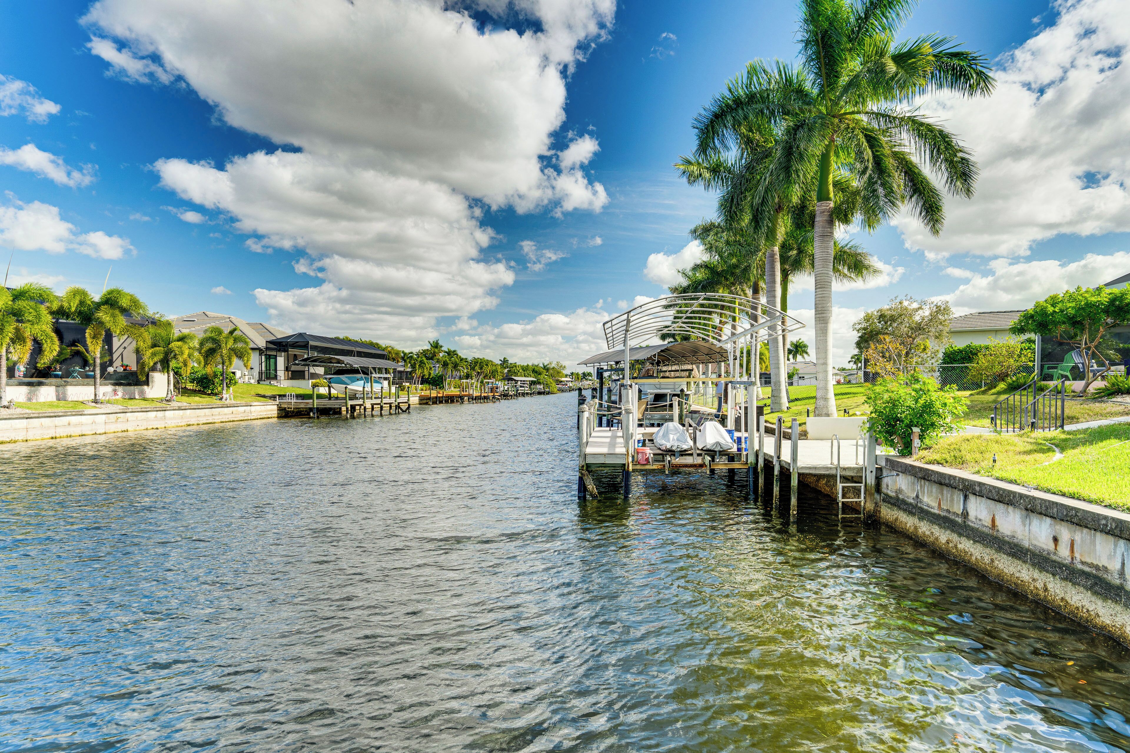 A waterfront hotel with a dock, palm trees, and a clear sky.