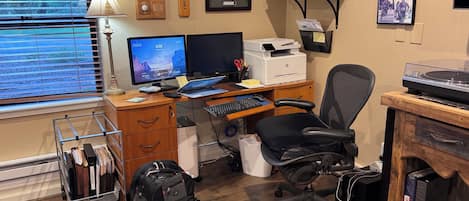 A home office with a desk, computer, chair, and various personal items.