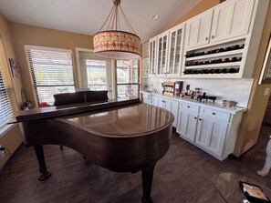 A piano in a room with a wooden floor, white cabinets, and a chandelier.