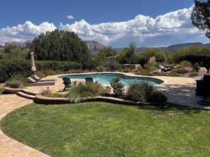 A backyard with a swimming pool, lounge chairs, and a view of mountains.