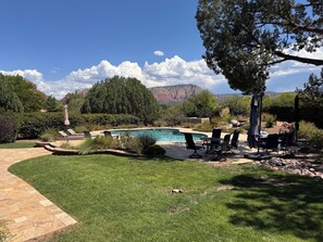 A backyard with a swimming pool, outdoor furniture, and a view of mountains.