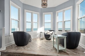 Enjoy a serene ocean view from the large bay window, paired with a comfortable seating area and soft gray walls.