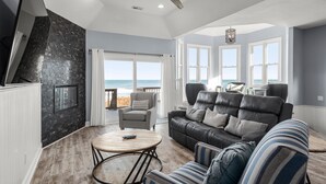 Un salon spacieux doté d’une grande fenêtre donnant sur la plage, d’un ventilateur de plafond et d’une cheminée.