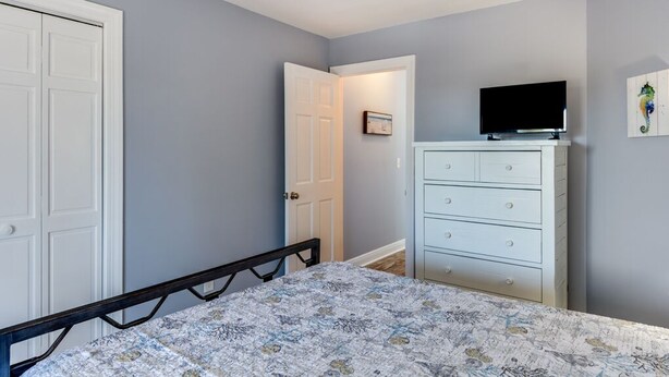Une chambre à coucher avec un lit, une commode, un téléviseur et une porte.