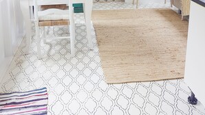 Una stanza con un tavolo da pranzo bianco, una sedia bianca, un televisore su un mobile in legno, un divano, una porta verde e un pavimento decorato.