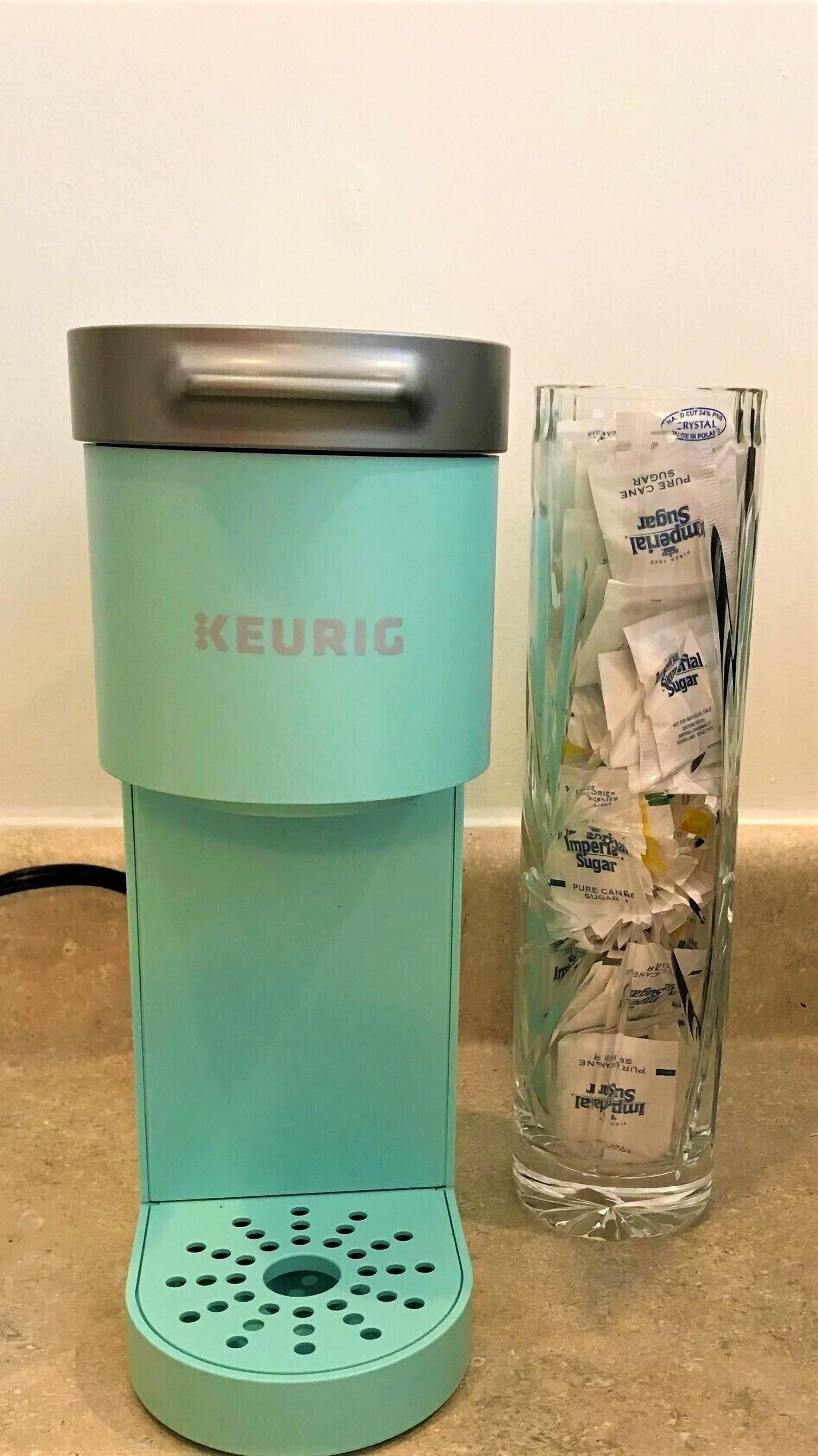 Une machine à café KEURIG de couleur turquoise, dotée d’une verseuse en verre remplie de capsules de café.