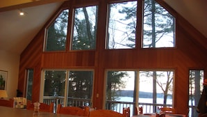 Un'ampia sala da pranzo con un grande tavolo di legno e sedie, ampie finestre che offrono vista su alberi e uno specchio d'acqua.