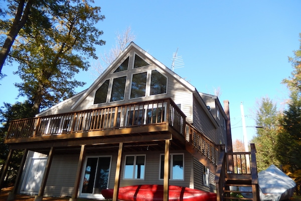 House facing lake with deck above, canoe and kayak stored on ground level.