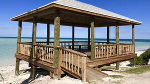 A wooden beach pavilion with a roof and a wooden deck, situated on a sandy beach with clear blue water in the background. - Paradise Found,GREAT LOCATION,free golfcart, dishwasher, sup, kayak, rain water  (Spanish Wells)