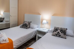 Camera d'albergo con due letti, ognuno dotato di una testiera bianca, un comodino con una lampada e uno specchio.