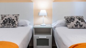 Ein Hotelzimmer mit zwei Betten, einem Nachttisch mit Lampe und einer kleinen Schublade.
