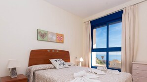 Un letto rifatto con cura, con una coperta a fiori e un cuscino con la scritta 'Fai un desiderio', e vista sul mare attraverso un'ampia finestra.