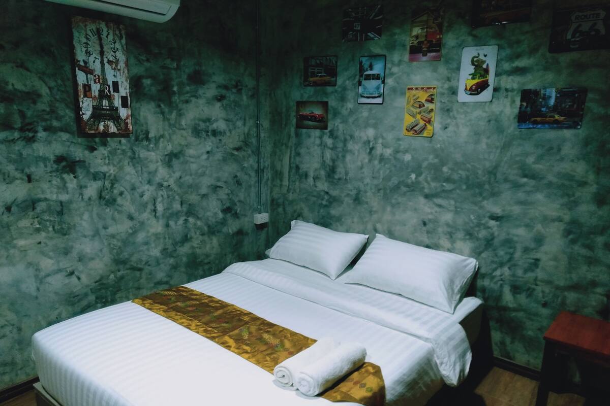 Una habitación con una cama, una mesita de noche de madera y una pared decorada con varios carteles.