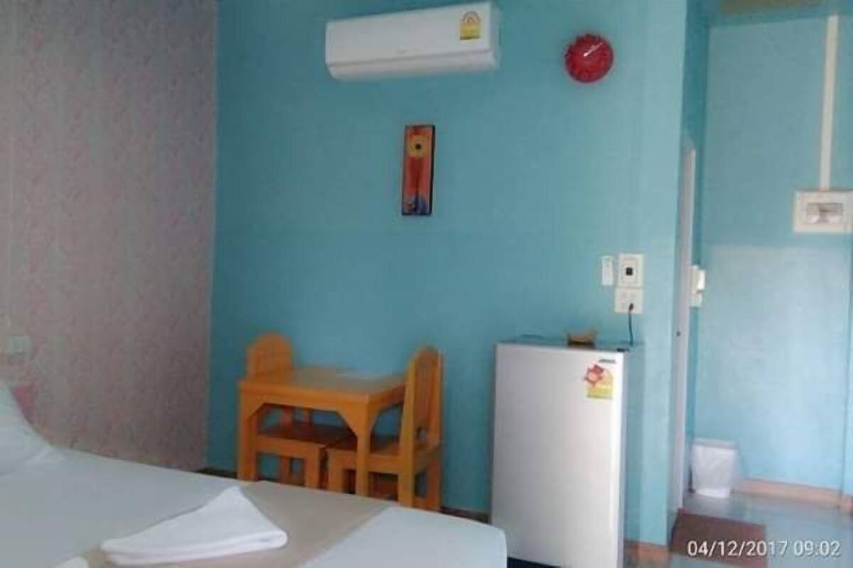 Una habitación con una cama, una mesita de madera, un refrigerador blanco y un aire acondicionado instalado en la pared.