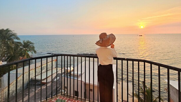 Eine Person auf einem Balkon mit Blick auf das Meer bei Sonnenuntergang.