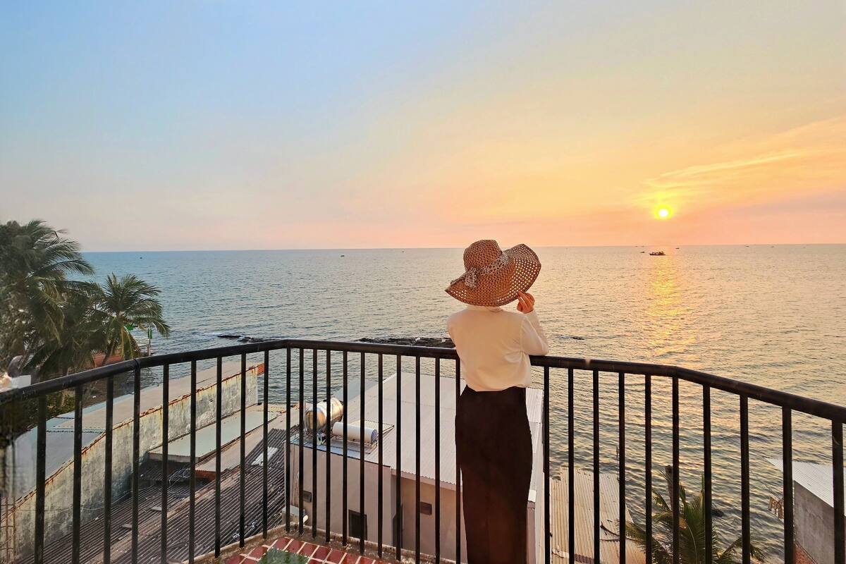 A person on a balcony overlooking the sea during sunset.