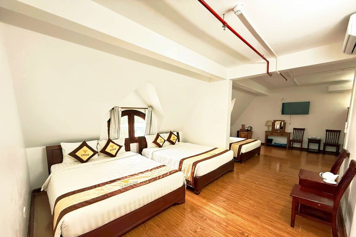 A hotel room with two beds, wooden flooring, a desk, and a chair.