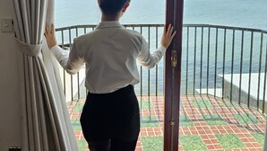 Eine Person steht neben einer Balkontür mit Blick auf das Meer.