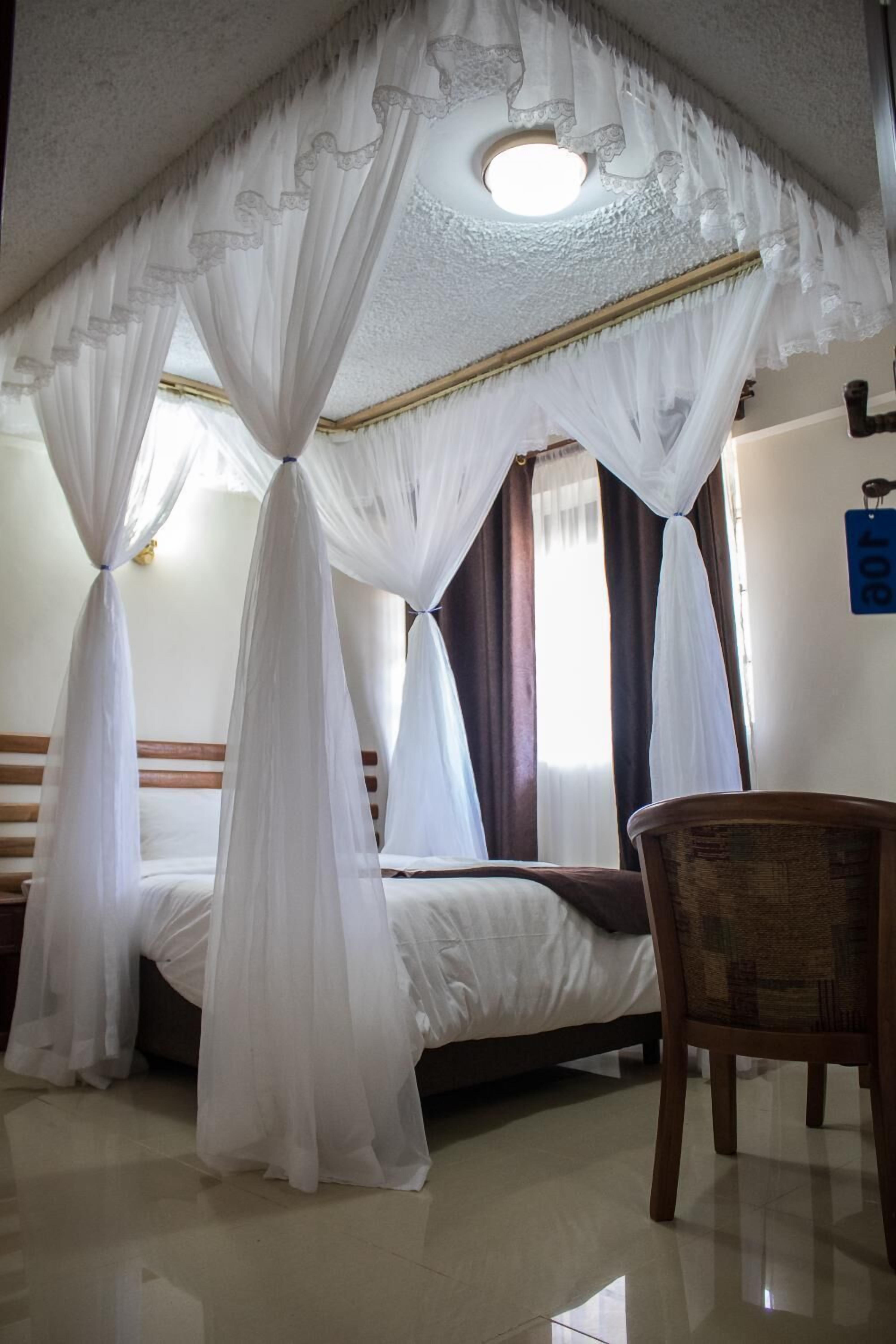 Una habitación con una cama bajo un dosel, una silla y un cartel en la pared.