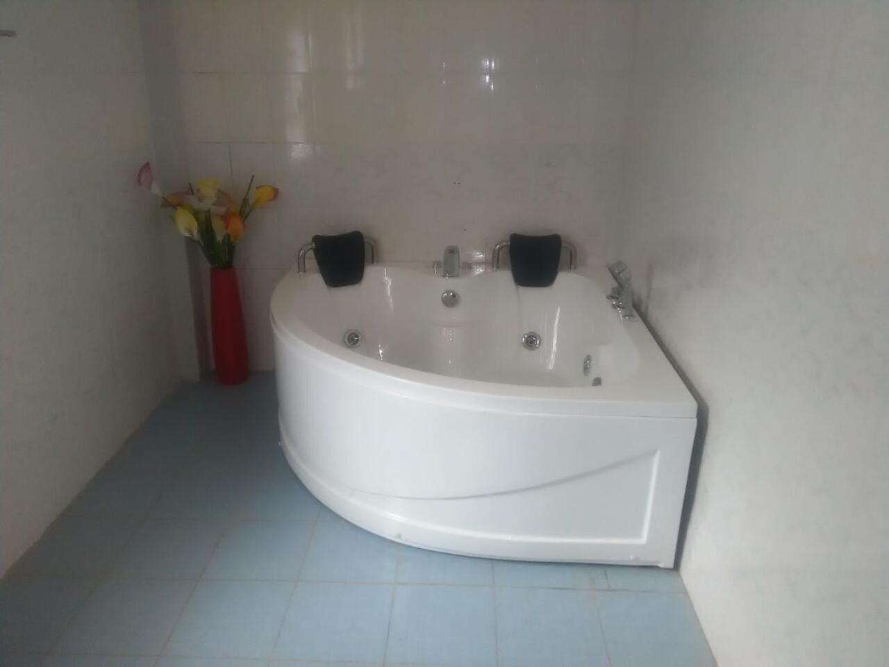 A bathroom with a white bathtub, two black towel racks, and a red vase with flowers on the floor.