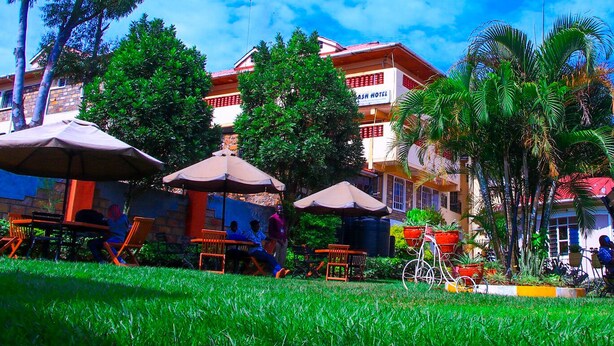 A hotel with outdoor seating, palm trees, and a clear blue sky. - Calabash Hotel (Migori)