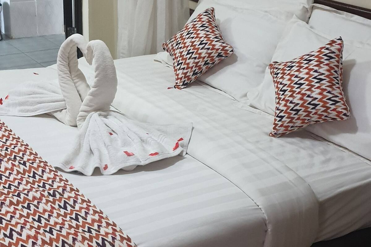 Ein Hotelzimmer mit einem Bett, weißer Bettwäsche, gemusterten Kissen und einem Vorhang.