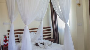 A four-poster bed with white drapes, a wooden headboard, and a bedside table with a vase of flowers. - Calabash Hotel (Migori)