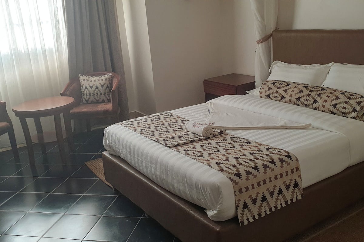 Ein Hotelzimmer mit einem großen Bett, einem kleinen Tisch, zwei Stühlen und einem Nachttisch.