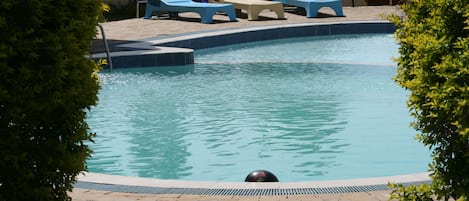 Una piscina al aire libre, sombrillas, sillones reclinables de piscina