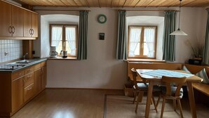 A kitchen with wooden cabinets, a dining table with chairs, and two windows with curtains. - "Zellerhorn" Ferienwohnung I°, 39 qm, extra Schlafzimmer° (Aschau im Chiemgau)