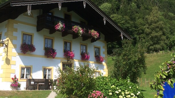 A traditional chalet with multiple windows, balconies with flower boxes, and a garden area with various plants and flowers. - "Zellerhorn" Ferienwohnung I°, 39 qm, extra Schlafzimmer° (Aschau im Chiemgau)