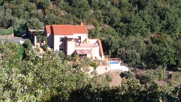 Ein zweistöckiges Haus mit rotem Dach, umgeben von dichtem Grün und Hügeln.