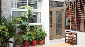 A building with a white exterior, a brown door, and a window with a metal grid. There are potted plants and a wooden bench outside. - JU Meet up with ocean (Hengchun)