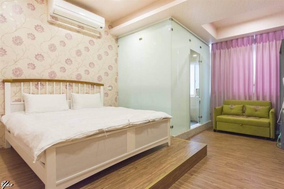 Un dormitorio con una cama, un sofá verde, un armario de vidrio y una cortina rosa.
