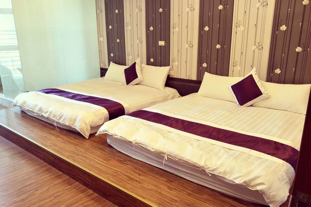 Habitación de hotel con dos camas, piso de madera y un diseño de papel tapiz a rayas.