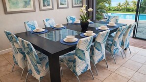 A dining area with a glass table, chairs with leaf-pattern upholstery, and a view of a pool and palm trees. - ChampionsGate, 9 Bed Superb Luxury Villa, Sleeps 34, South Facing Pool/Spa. (ChampionsGate)