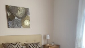 Un letto ben rifatto con una coperta a motivo circolare, un comodino con una lampada e un'opera d'arte appesa sopra il letto.