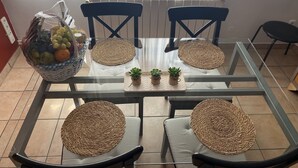 Zona pranzo con tavolo in vetro, due sedie blu e sottopiatti intrecciati.