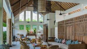 A spacious living area with wicker furniture, a wooden wall panel, and large windows. - Abaca Villas (Seminyak)