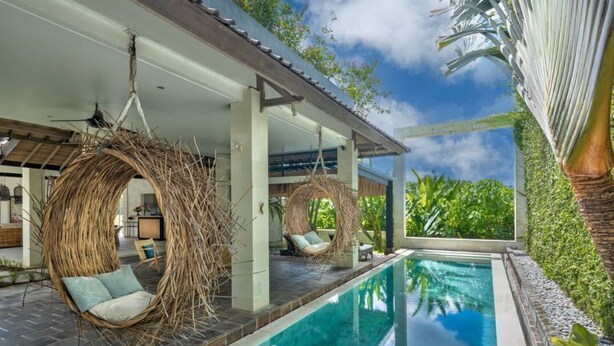 A poolside area with a clear blue pool, wicker chairs, and a covered seating area with a view of lush greenery. - Abaca Villas (Seminyak)