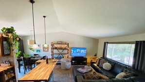 Una sala de estar acogedora con una mesa de comedor de madera, un sofá de cuero negro y un televisor.