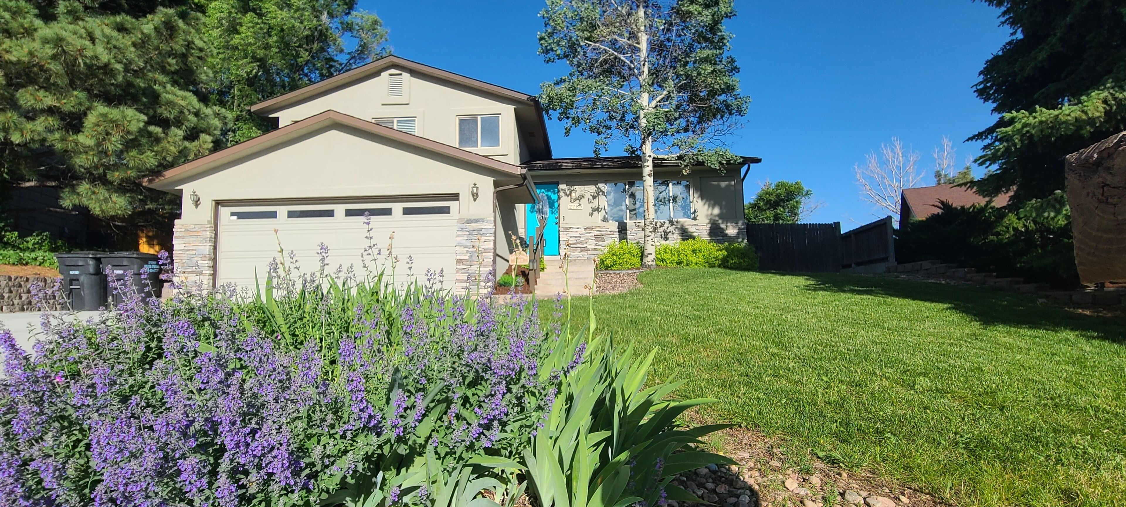 A two-story house with a garage, surrounded by a well-maintained lawn and flowering plants.