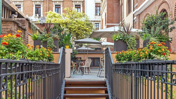 A courtyard with a wooden staircase leading to an outdoor seating area, surrounded by brick buildings and potted plants. - Albergo Etico Roma (Rome)