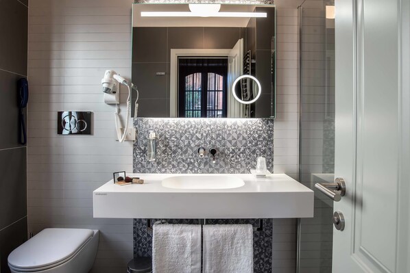 Un baño moderno con un lavamanos blanco, un espejo con luz de aro y un inodoro.