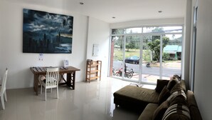 A living room with a large window, a sofa, a wooden table, and a chair. - Sleep Inn (Koh Samui)