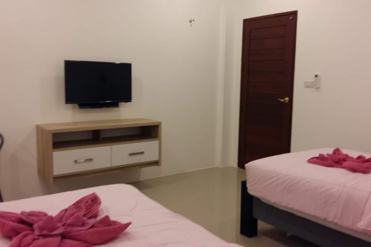 Un dormitorio con dos camas, un televisor en la pared, un armario de madera y una puerta.