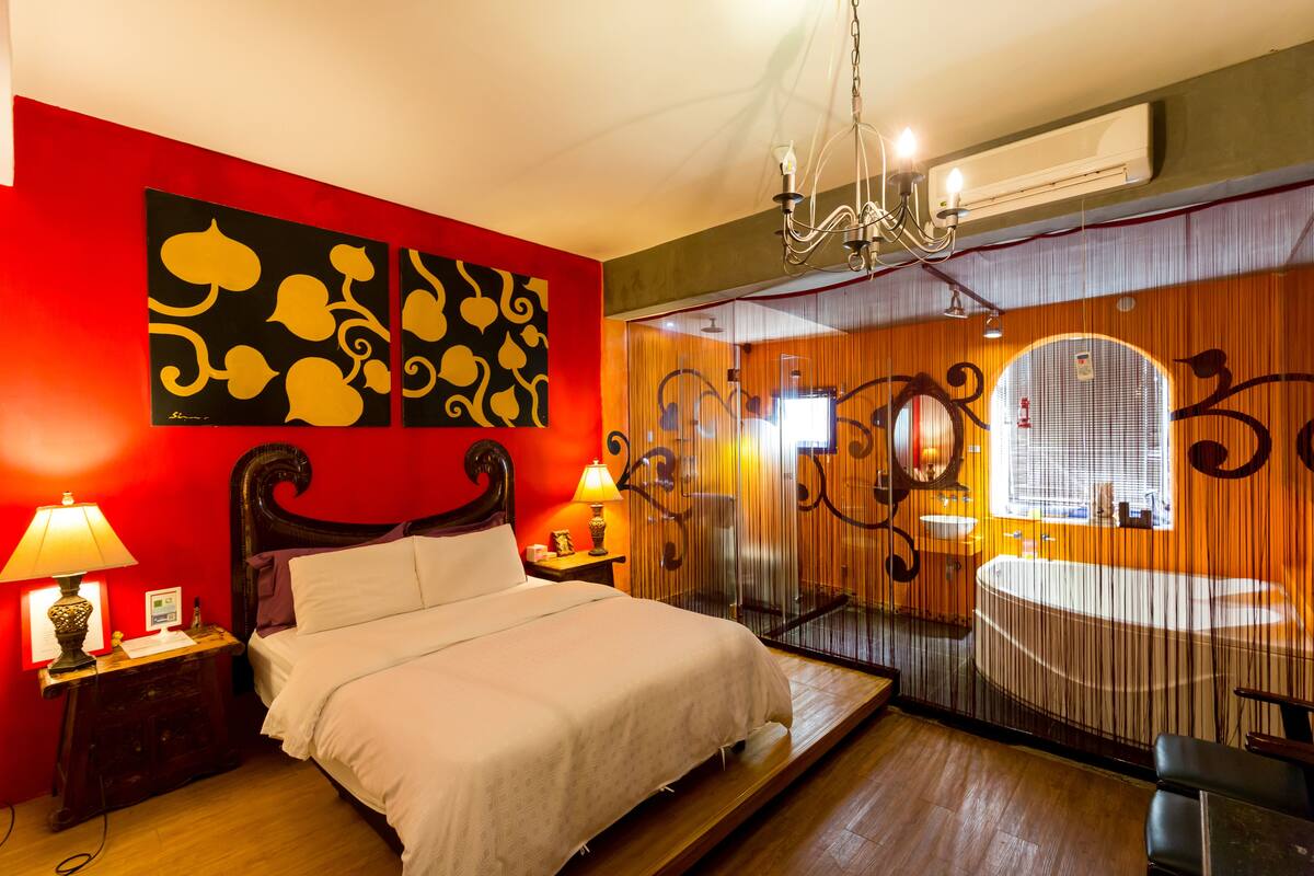 Habitación de hotel con cama, lámparas de noche, candelabro, ventana con cortinas y baño con bañera.