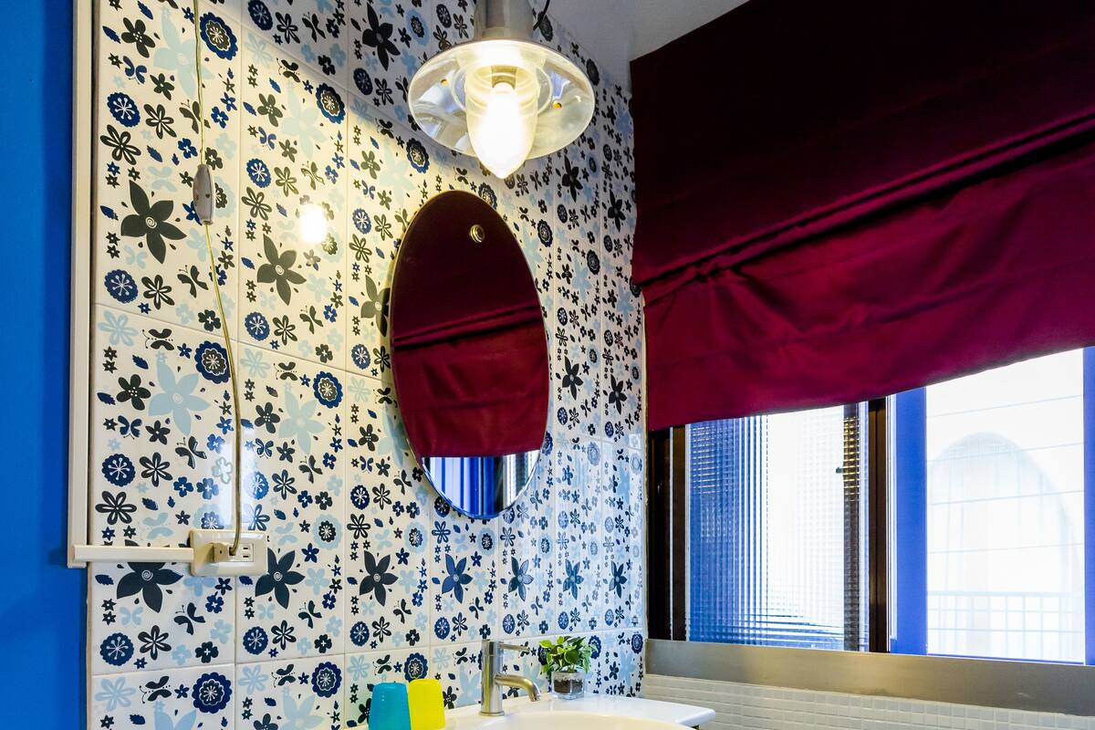 Un baño con un salpicadero de azulejos con motivos florales, un lavamanos blanco con grifo dorado y un suelo de azulejos azules.