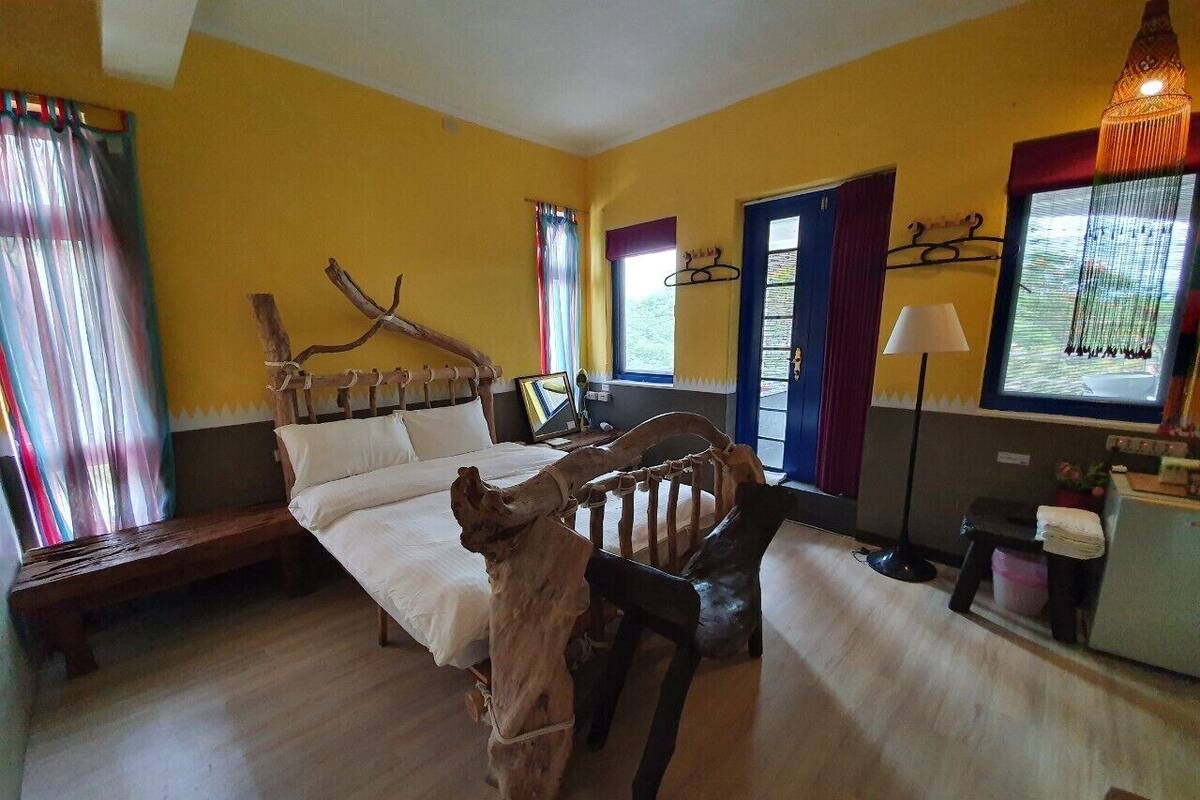 Un dormitorio con cama, una silla de madera, un banco, un escritorio y una lámpara.