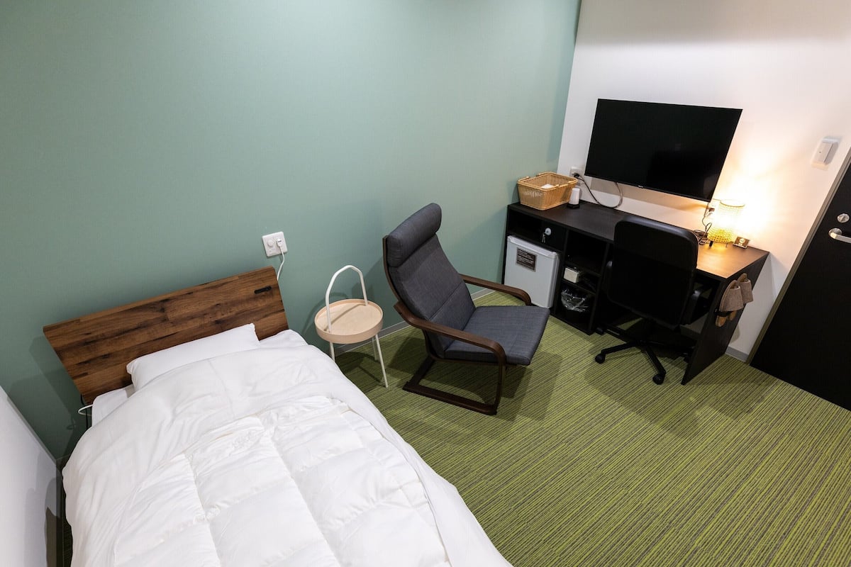 A hotel room with a bed, a desk, a chair, a television, and a small refrigerator.